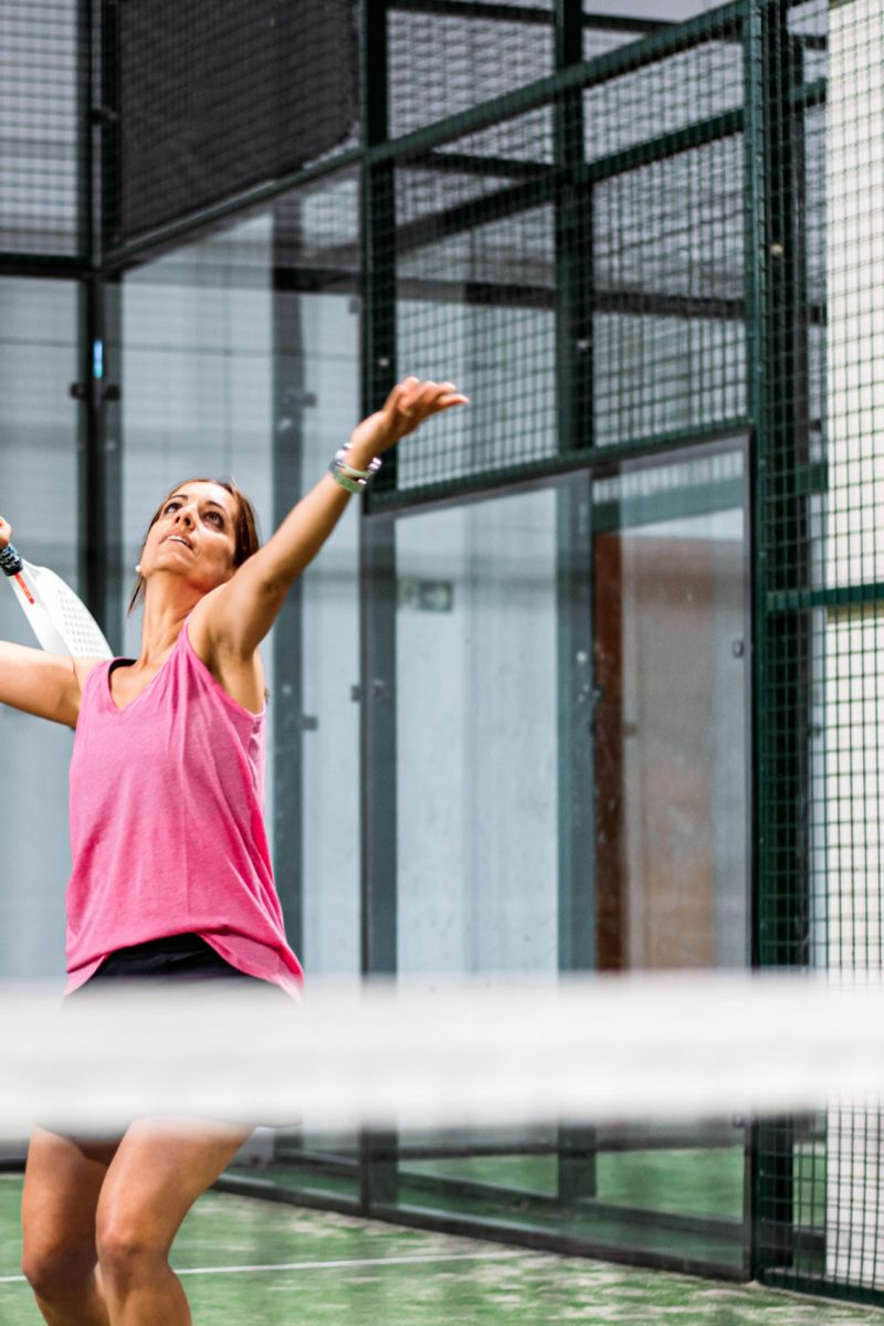 Woman playing padel in a green grass padel court indoor behind the net